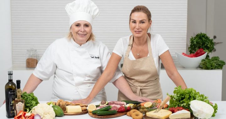 Two female chefs with variety of fresh ingredients in a kitchen setting, showcasing culinary preparation.