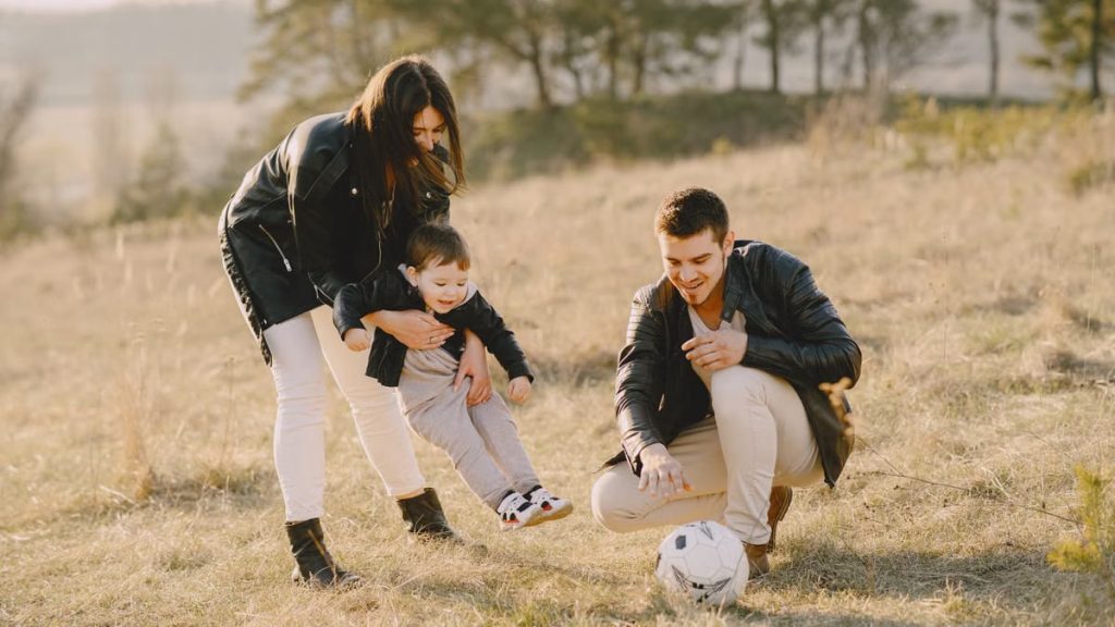 A happy family playing with a soccer ball in a grassy field on a sunny day.