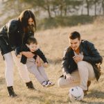A happy family playing with a soccer ball in a grassy field on a sunny day.