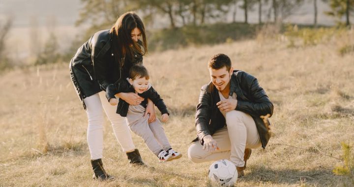 A happy family playing with a soccer ball in a grassy field on a sunny day.