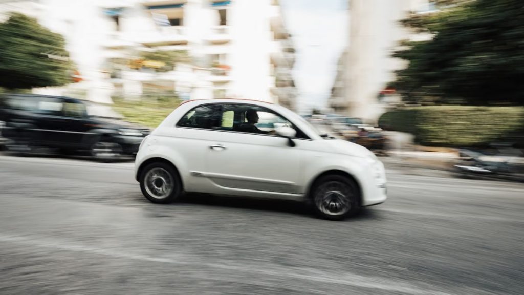 Dynamic capture of a compact white car speeding through a city street with motion blur effect.