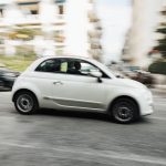 Dynamic capture of a compact white car speeding through a city street with motion blur effect.