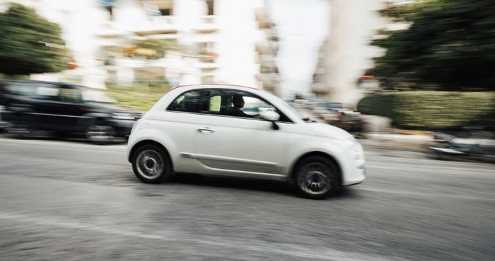 Dynamic capture of a compact white car speeding through a city street with motion blur effect.